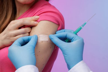 Doktor, pembe ve mavi arkaplandaki aşıdan sonra kadının eline yapıştırıcı yapıştırıyor. Aşı ve bağışıklık merkezi hizmet konsepti, modern tıp