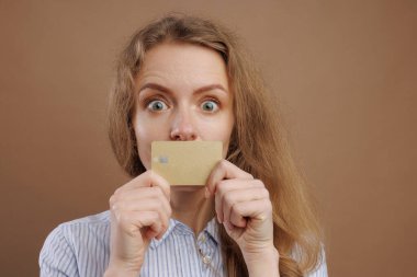 Şaşırmış bir kadın altın banka kartıyla ağzını kapatıyor, bej arka planda, online ödemeler, NFC