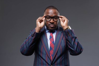 Kendine güvenen iş adamı gözlük takıyor, şık çizgili takım elbise ve kravat takıyor. Profesyonel portre, liderlik, zeka, başarı, şirket tarzı ve odaklanma konsepti. Koyu arkaplan.