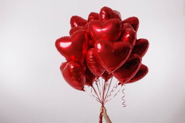 Temiz beyaz bir arkaplan karşısında büyük bir demet kırmızı kalp şeklinde balon tutan bir el. Aşkı, aşkı ve kutlamaları simgeliyor..