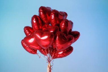 Bir grup kırmızı kalp şeklinde balonu canlı mavi gökyüzüne karşı tutarak, aşkı, kutlamayı ve neşeyi sembolize ediyor..