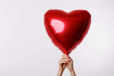 Temiz beyaz bir zemin üzerinde parlak kırmızı bir kalp şeklinde balon tutan bir el. Aşkı, aşkı ve kutlamaları simgeliyor..