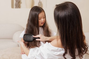 Anne, evde uzun saçlarını tarıyor. Aile bakımını, şefkati ve her gün bağ kurma anını ayarlıyor..
