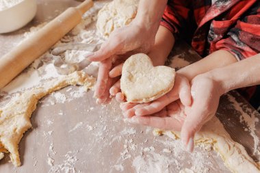 Anne ve çocuğun birlikte pişirmesi, kalp şeklinde hamuru tutan eller, aile bağları, ev yapımı pastalar, sıcak mutfak sahnesi, un kaplı eller..