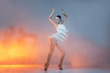 Beyaz püsküllü elbiseli zarif Latin dansçı zarif ve kendine güvenen sanatsal ışıklandırmada dinamik bir hareket sergiliyor..