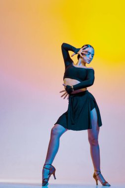 Siyah elbiseli zarif dansçı parlak bir arka planda Latin Amerika dansları yapıyor..