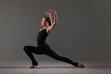 Siyah elbiseli kadın dansçı gri stüdyoda çağdaş Latin dansı pozu veriyor.