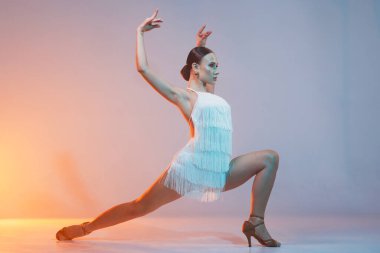 Beyaz püsküllü elbiseli zarif Latin dansçı zarif ve kendine güvenen sanatsal ışıklandırmada dinamik bir hareket sergiliyor..