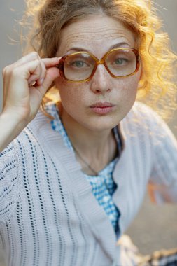 konsept görme bozukluğu, çilli genç bir kadın büyük vintage gözlük takıyor kameraya tuhaf bir şekilde bakıyor örgü kazak ve kareli elbiseler giyiyor..