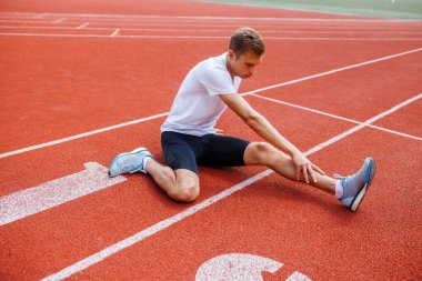 Koşu pistinde gerinen sporcu, antrenman veya yarışmaya hazırlanıyor, sporda esneklik ve sakatlığı önlemeye odaklanıyor