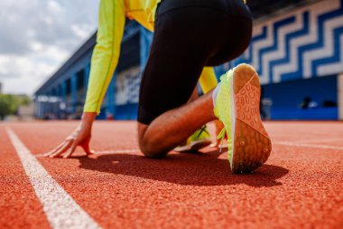 Başlangıç çizgisinde sprinter, açık havada yarışmaya hazır, parlak spor giyim ve çivili koşu ayakkabıları giyiyor, düşük açıyla yakalandı.