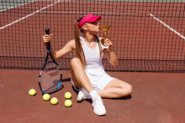 Genç bayan tenisçi zaferi kutluyor, dışarıda kupayı öpüyor..