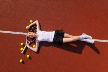 Genç bayan tenisçi dinlenirken raket ve toplarla poz veriyor, antrenmandan sonra dinleniyor..