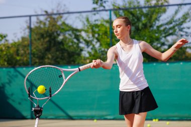 Sahada tenis antrenmanı yapan genç bir kız antrenman yardımı alıyor, açık hava antrenörlüğü sırasında odaklanıyor..