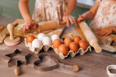 Çocuklar birlikte kurabiye pişiriyor, hamuru yuvarlıyor ve kırsal bir masada taze yumurta ve un ile kesiyor..