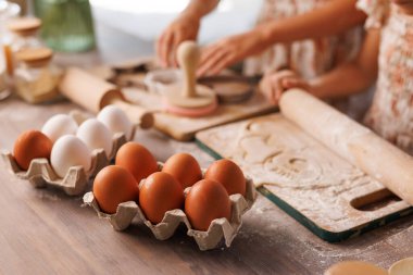 Çocuklar taze yumurta pişiriyor, hamuru yuvarlıyor ve un ahşap mutfak yüzeyinde şekiller kesiyor..