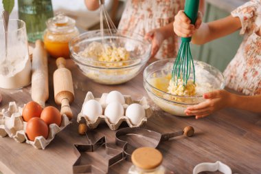 Çocuklar taze yumurtalar, pişirme aletleri ve un ile çevrili cam kaselerde hamur çırpar..