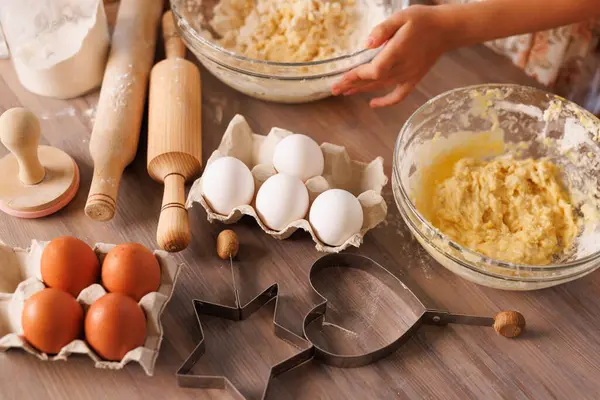 Çocuklar taze yumurtalar, pişirme aletleri ve un ile çevrili cam kaselerde hamur çırpar..