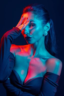 Canlı kırmızı-mavi ışıklı, gösterişli tarzı, cazibesi ve tavırları olan kendinden emin bir kadının cesur stüdyo portresi..