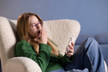 Uykulu genç kadın, elinde akıllı telefon tutarken esniyor. Evde geçirdiği ekran saatinden sonra yorgun ve uykulu hissediyor..