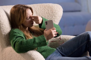 Akıllı telefon ekranına bakarken gözlerini ovuşturan hayal kırıklığına uğramış genç bir kadın dijital göz yorgunluğu yaşıyor..