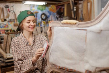 Gülümseyen kadın döşeme ustası atölyedeki klasik koltukları zımparalıyor, mobilyaları özenle ve titizlikle restore ediyor..