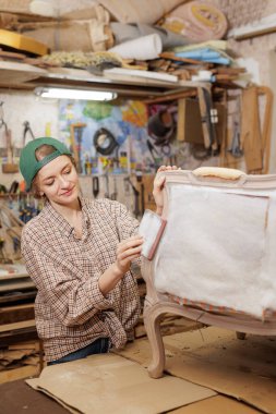 Genç kadın döşeme ustası, atölyedeki klasik sandalyeyi zımparalıyor, mobilyaları hassasiyetle ve yaratıcılıkla restore ediyor..