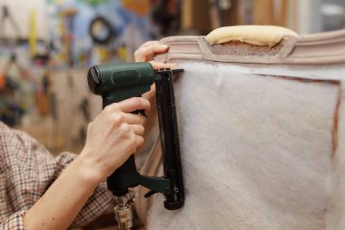 Döşeme işi sırasında eski bir koltuğa yastık takmak için pnömatik zımba kullanan ellerin yakın çekimi..