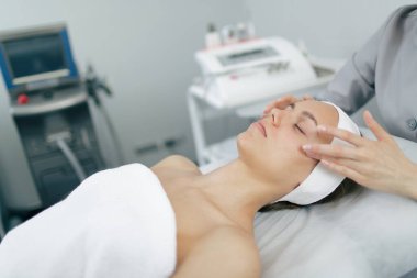 Genç bir kadın güzellik kliniğinde yüz masajı yaptırıyor. Rahatlama ve parlaklık için profesyonel cilt bakımı terapisi.
