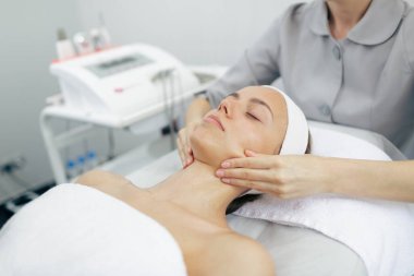 Kadın güzellik salonunda cilt gençleştirme ve rahatlama tedavisi için profesyonel yüz masajı yaptırıyor..