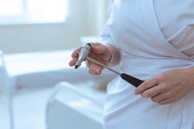 Tıbbi bir odada, bir hastanın nörolojik muayenesine hazırlanan bir doktor refleks çekici tutuyor..