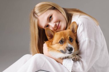 Sarışın kadın sıcak bir anda sakin ve bağlı bir şekilde otururken Corgi köpeğine sevgiyle sarılıyor..