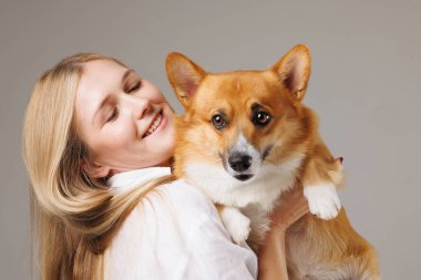 Sevimli Corgi köpeğini kucağında tutan neşeli genç bir kadın, hem mutlu hem de sevecen görünüyor..