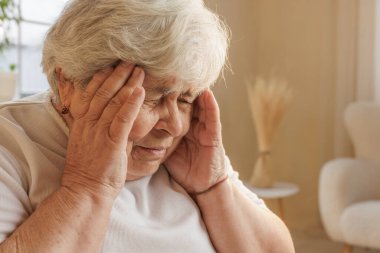 Yaşlı bir kadının şakaklara dokunduğu, baş ağrısı ya da migrenden muzdarip olduğu, gözleri acıdan kapandığı yakın plan..