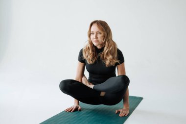 Kendine güvenen bir kadın kaldırılmış nilüfer yogası yapıyor. Kapalı alanda poz veriyor. Denge, güç ve sakin bir odak noktasını birleştiriyor..