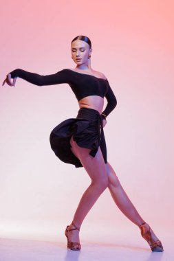 Dinamik hareketli zarif Latin dansçı, pembe gradyan arka planda siyah elbiseyle dramatik bir poz veriyor..