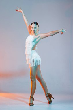 Kendine güvenen Latin dansçı, stüdyo sahnesinde dramatik turuncu-mavi ışık altında püsküllü bir elbise giymiş..