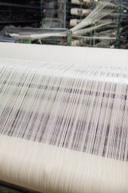 Modern bir kumaş fabrikasında dokuma tezgahında beyaz ipliklerle otomatik tekstil üretimi.