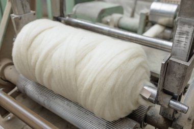 Bir tekstil fabrikasında iplik üretiminde dönen bir makineye sarılı büyük bir rulo yün iplik..