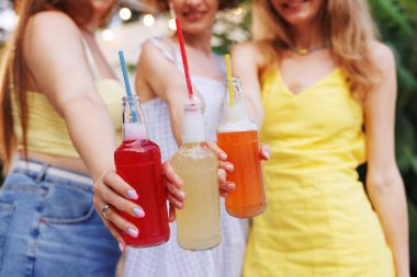 Açık hava kutlaması sırasında ellerinde renkli köpüklü içkiler olan üç genç kadının yakın çekimi..