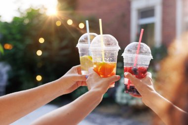 Elleri renkli yaz içkilerini plastik bardaklarda meyve dilimleriyle tutarken gün batımında açık havada kadeh kaldırırken..