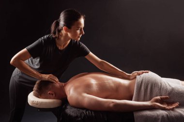 Profesyonel terapist, erkek müşteriye yüz üstü uzanıp vücut masajı yapıyor..