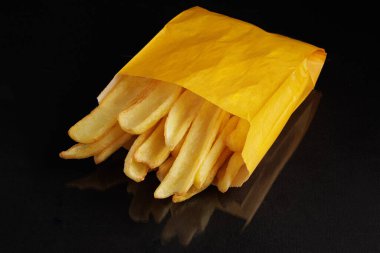 Siyah arka planda sarı bir kese kağıdında çıtır patates kızartması. Klasik fast food konsepti..