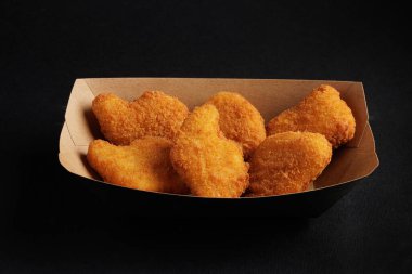 Koyu bir arka planda karton tepside servis edilen çıtır tavuk nuggetları, mükemmel bir fast food atıştırmalığı..