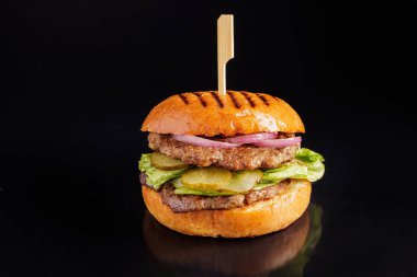 Kızarmış ekmeğin içinde turşulu, marullu, soğanlı sulu ızgara sığır burger, yakın plan görüş..