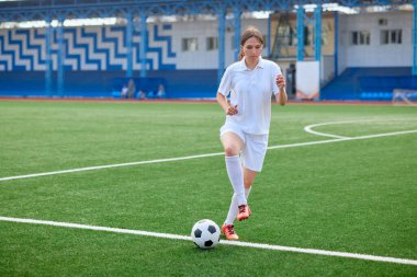 Aktif eğitim sırasında yeşil sahada topu kontrol eden beyaz üniformalı kadın futbolcu..