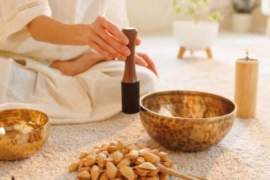 Tibet şarkı kasesi kullanan bir kadının evde huzurlu, sıcak bir seansta iyileşme sürecinde çekilmiş yakın çekimi..