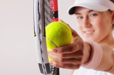 Tenis oyuncusu topu ve raketi yakın çekimde tutuyor, el ve teçhizata odaklanıyor, sportif ve enerjik bir hava yaratıyor..