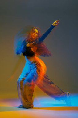 Canlı hareket bulanıklığı içinde caz funk dansçısı, renkli bir stüdyoda akan ışıklar ve şehir enerjisiyle cesur bir poz veriyor..