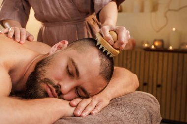 Erkek müşteri, huzurlu bir kaplıcada saç fırçası kullanarak kafa masajı yapıyor. Rahatlamayı ve kafa gerginliğini azaltır..